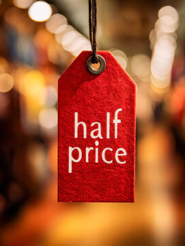 Red discount tag with half price text hanging against a warm bokeh background symbolizing a special sale or promotional offer in a retail environment