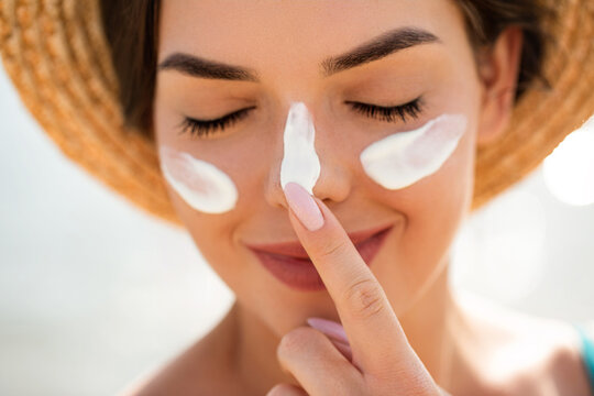 Beautiful woman applying sunscreen on nose with finger smiling with closed eyes in bright sunlight showing detailed skincare routine and summer sun protection concept