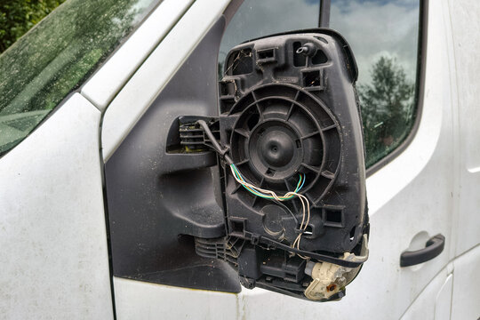 Broken side mirror on a white delivery van with exposed wiring and missing glass, parked outdoors after vehicle damage