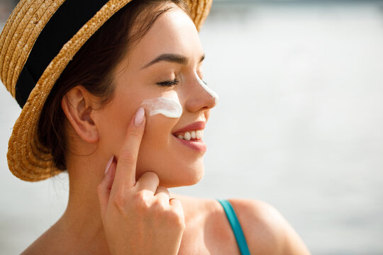 Beautiful woman applying sunscreen on cheek in profile with closed eyes enjoying sunlight with glowing skin and calm summer skincare sun protection concept