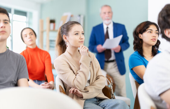 Young girls and guys audience listen to lecture, mature man teacher in background. Social projects for young people. Prevention of addictive behavior, information support for youth in bullying