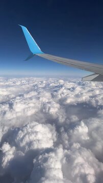 Airplane wing with a distinctive blue winglet flying over fluffy white cumulus clouds in a clear blue sky. High altitude aerial view.