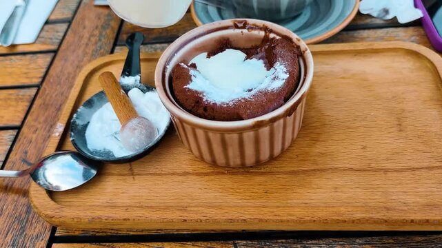 A decadent chocolate lava cake in a ceramic ramekin being poured with fresh cream, served on a rustic wooden tray with powdered sugar, creating an appetizing food video perfect for culinary content.