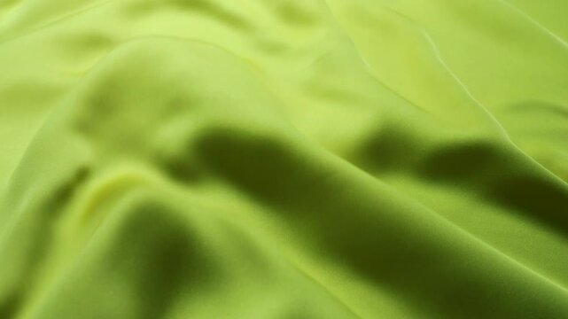 Natural silk fabric of lemon green color waving in the wind. Soft abstract waves of textile creating a smooth motion background. Elegant satin material with a subtle light and shadow play.
