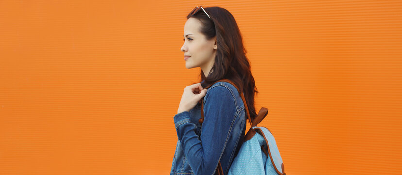 young woman student in casual with backpack against orange wall background