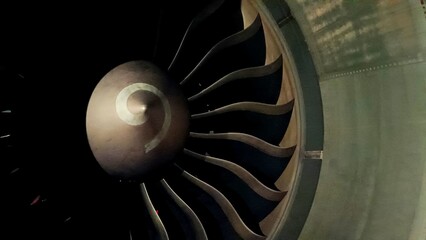 Close-up of a turbofan aircraft engine fan in the dark, showcasing symmetrical blades and spinner cone © Sarmiko.id