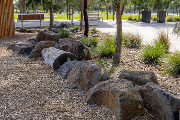 A row of natural basalt and granite boulders used as landscape edging along a garden bed border in a suburban park in Australia, with native ornamental grasses, woodchip mulch,  eucalyptus trees © Doublelee