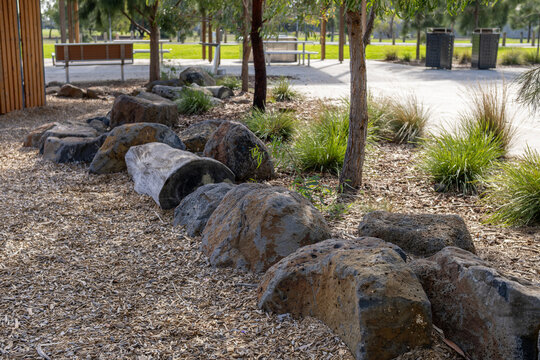 A row of natural basalt and granite boulders used as landscape edging along a garden bed border in a suburban park in Australia, with native ornamental grasses, woodchip mulch,  eucalyptus trees