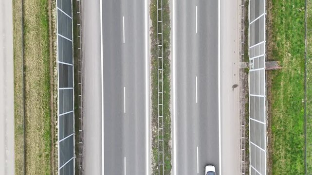 Aerial view of cars driving on a divided highway, showcasing the continuous movement of vehicles along the road with green grass and barriers lining the sides