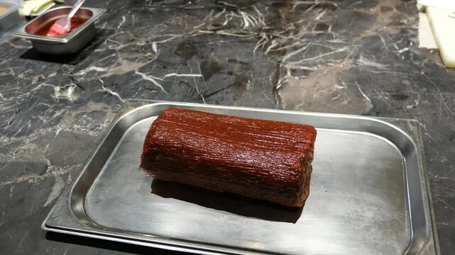 Static close up of a beautifully marinated and prepared meat roll resting on a stainless steel tray with dark background for culinary arts and professional food styling.