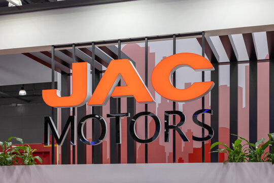 JAC MOTORS brand logo signage at a commercial automotive exhibition stand. Large orange and black corporate lettering on a decorative background. Astana, Kazakhstan - May 30, 2024