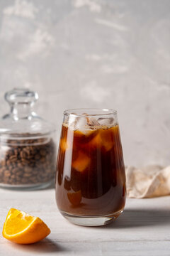 Coffee with orange juice bumble in a tall glass with ice on a light background with coffee beans, fruits and morning shadows