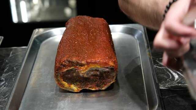 Chef preparing a large marinated roast meat on a metal tray in a professional restaurant kitchen focusing on food preparation and gourmet cooking techniques for culinary documentaries