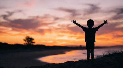 Fototapeta premium Silhouette of a young child with arms outstretched at sunset.