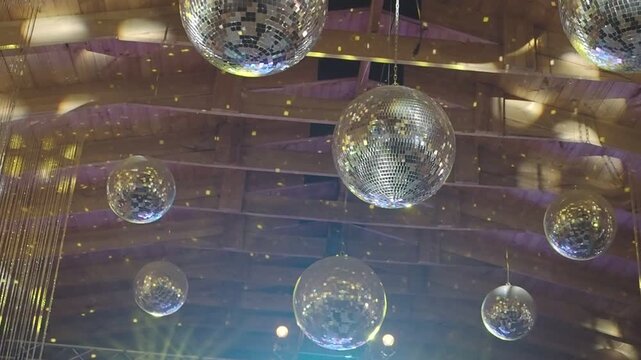 Shining disco balls hang suspended, catching light. Reflections dance across mirrored surfaces below. Warm tones glow from unseen stage lights. No people visible, no animal or plant shown