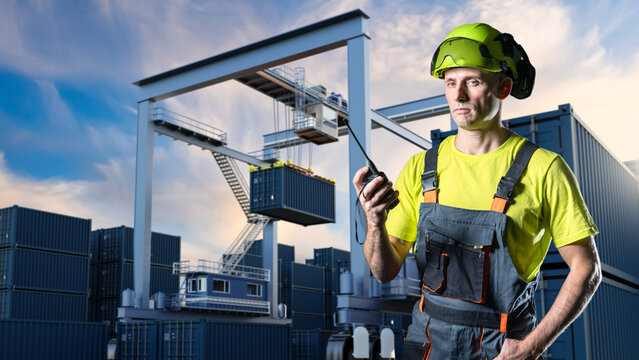 Port logistics, Container terminal. Dock worker in safety helmet communicates by radio while supervising cargo container lifting with gantry crane, coordinating loading operations at shipping yard.