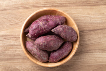 Raw organic purple sweet potatoes in a wooden bowl on wooden background, Table top view