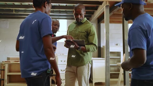 Man in green showing tablet in woodshop, crew leaning, tapping plan, confirming, dispersing