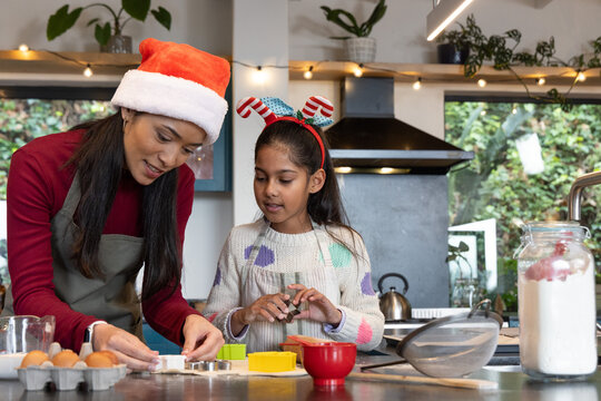 Indian mother and daughter in Santa hat and fun headband baking cookie cutters on kitchen counter