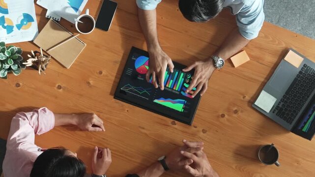 Top aerial view of business man present financial graph to group of smart investors. Professional male leader analyze graph and explain marketing idea by using tablet on meeting table. Convocation.