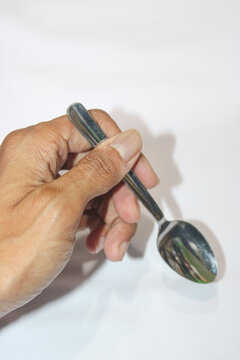 Hand holds silver spoon against plain white background