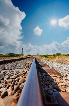Low-Angle View of Railway Track leading to the horizon Under Sunny Sky with white clouds.