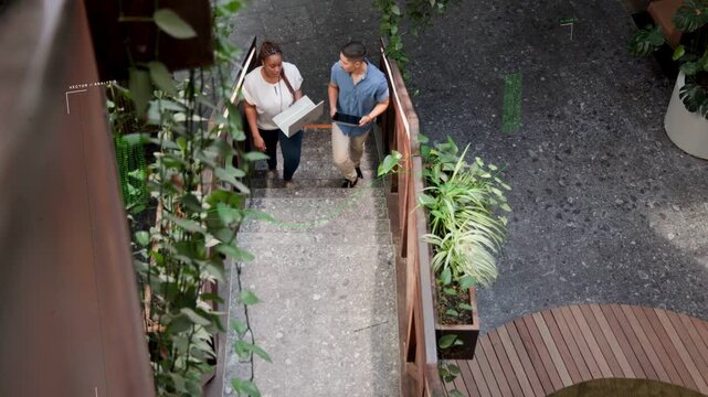 Vertical video: 2 IT staff with box on atrium steps tapping tablet showing overlay confirming route