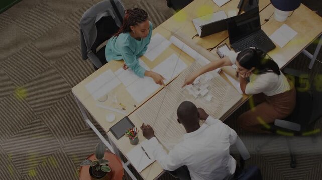 Woman in teal top pointing at blueprint and leading team into arranging cards for office design