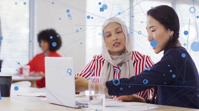 2 women working one reaching laptop and starting business review with blue network overlaying desk