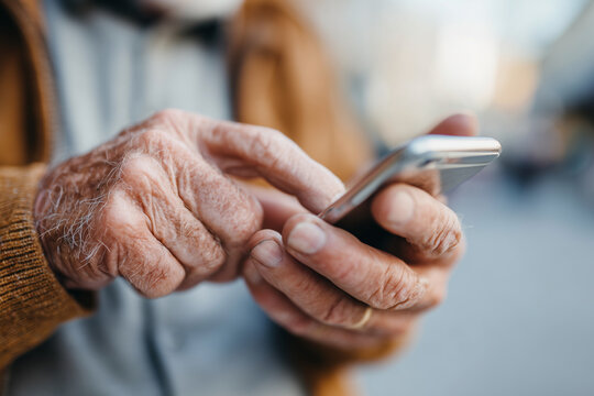 Close-up of elderly hands typing on smartphone. Wrinkled skin shows age and experience. Fingers press screen with focus and care. Shows modern seniors embracing technology