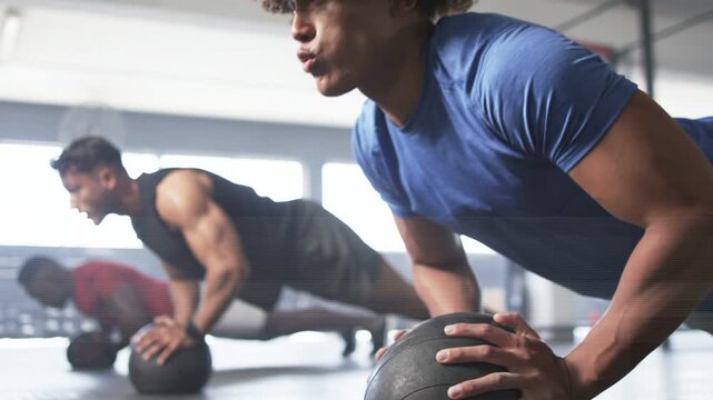 Partners doing fitness pushups in gym gripping 15 lb med ball, lowering then pressing for strength