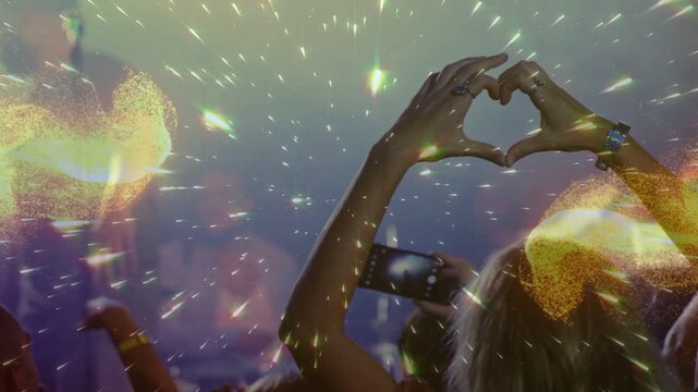 Woman forming heart hands to music at concert, smartphone recording, particles pulsing around hands