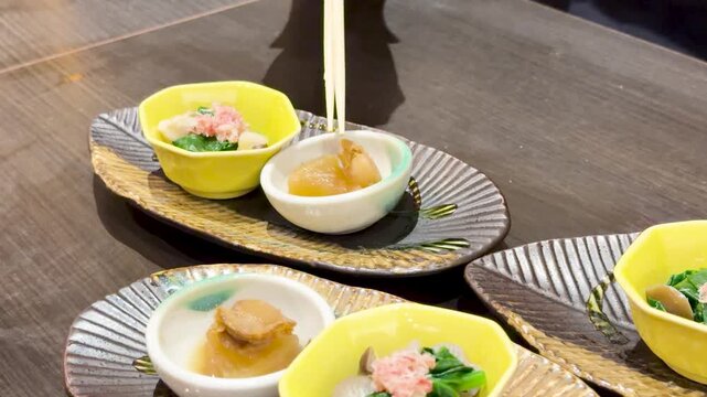 Chopsticks lifting traditional japanese appetizer from small ceramic bowl in restaurant setting with shallow depth of field.