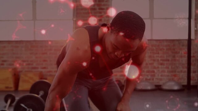 Vertical video: Reaching to grip dumbbell, male trainee in black tank rowing for strength at gym