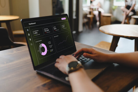 A close-up view of a person typing on a laptop that displays a generic business dashboard with financial charts and analytics for data monitoring.