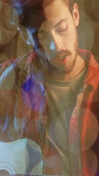 Man strumming acoustic guitar, singing for music practice, camera opening, bokeh drifting around