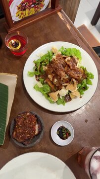 a plate of gado - gado, Indonesian traditional food, containing tofu, tempeh, vegetables, potatoes, boiled eggs, served with peanut sauce and crackers on top on the wooden table. Indonesian salad