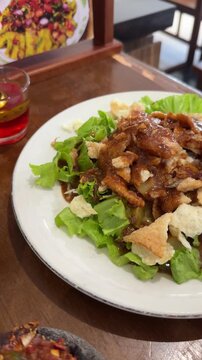 a plate of gado - gado, Indonesian traditional food, containing tofu, tempeh, vegetables, potatoes, boiled eggs, served with peanut sauce and crackers on top on the wooden table. Indonesian salad
