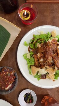 a plate of gado - gado, Indonesian traditional food, containing tofu, tempeh, vegetables, potatoes, boiled eggs, served with peanut sauce and crackers on top on the wooden table. Indonesian salad