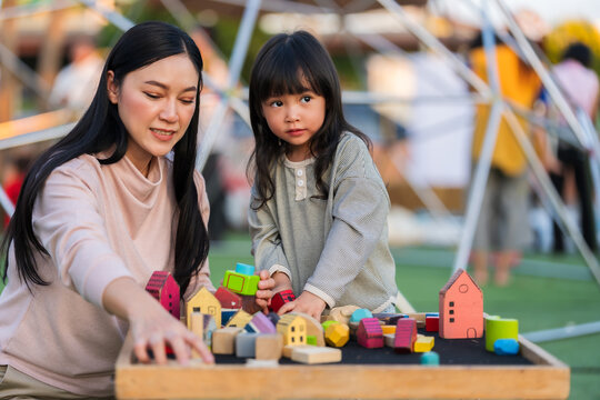 mother and preschool child girl playing with wooden toy block at outdoor