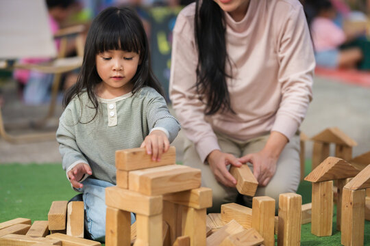 mother and preschool child girl playing with wooden toy block at outdoor