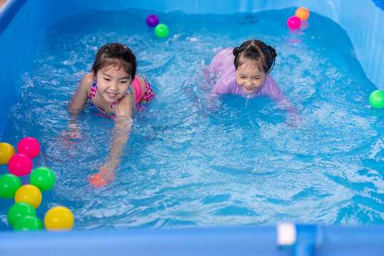 happy preschool child girl playing together with her sister in outdoor portable swimming pool in backyard