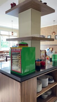 Tangerang, Indonesia on 18 April 2026: a self-service station in an Indonesian restaurant called Bumbu Pekalongan featuring a tin display case filled with Agung brand white crackers (kerupuk)