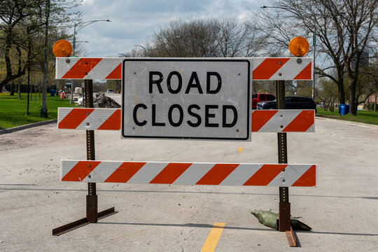 Horizontal photo of a 'Road Closed' sign on an orange barricade, blocking access to a closed road, indicating detours or construction work in progress