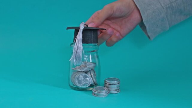 Financial planning for university featuring hand crowning coin jar with graduation hat on teal backdrop