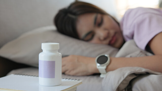 Young adult woman black asia people take herbal CBD pill bottle lying down on soft cozy bed deep sleep aid calm. Waking up happy serene relax drug anti aging good health care fall asleep till morning.