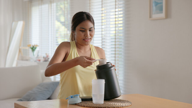 Young adult gen z active woman drink whey protein shake boost bottle diet food gain build muscle after home workout. health care black asia people happy relax sport protect aging life weight loss.