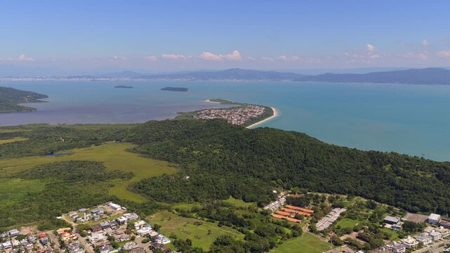 Drone glide over Praia da Daniela with calm bay and surrounding hills in Florianopolis.