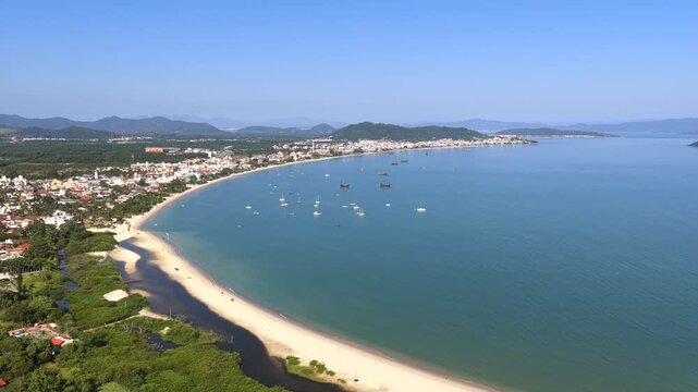Praia da Cachoeira do Bom Jesus in Florian&oacute;polis Santa Catarina Brazil on Atlantic Ocean with calm bay, sandy shoreline, and Serra do Mar mountains in background, drone descent