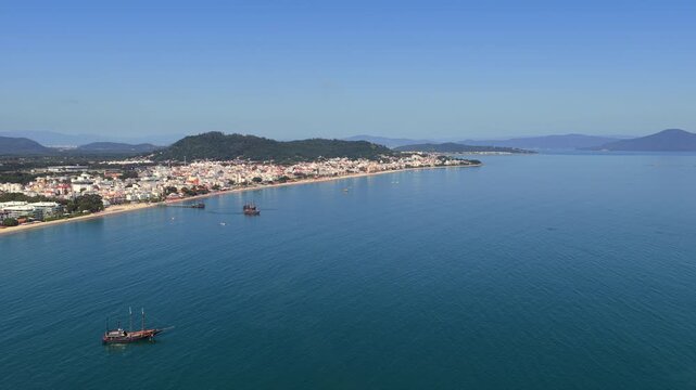 Pirate themed tourist schooner in Canasvieiras bay Florianopolis municipality Santa Catarina state South region Brazil navigating coastal waters near urban shoreline, drone forward glide towards beach